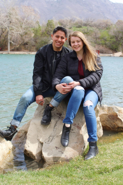 Aaron Cruz Morales and his wife sitting on a rock next to a body of water.