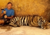 Lee Daniels sits next to a full-grown tiger, while holding its tail.