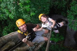 James Oldroyd and his young daughter ride a zipline through a green and thick jungle.