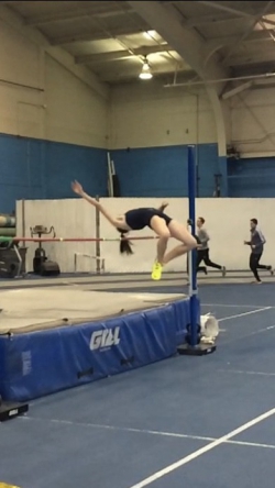 Rebecca completes a high jump over a pole. She is mid jump, bending backwards over the pole while completely airborne.