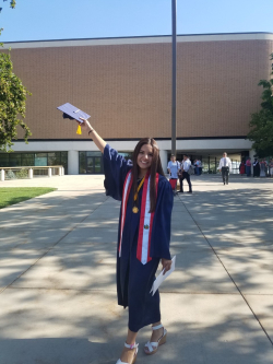 Brenda Tidwell holding her graduation cap up high, dressed in graduation robes in front of the Marriott Center.