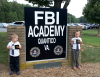 Two young boys stand in front of the FBI Quantico sign.