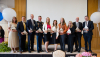 10 men and women stadning in a line on a stage and holding awards in their hands